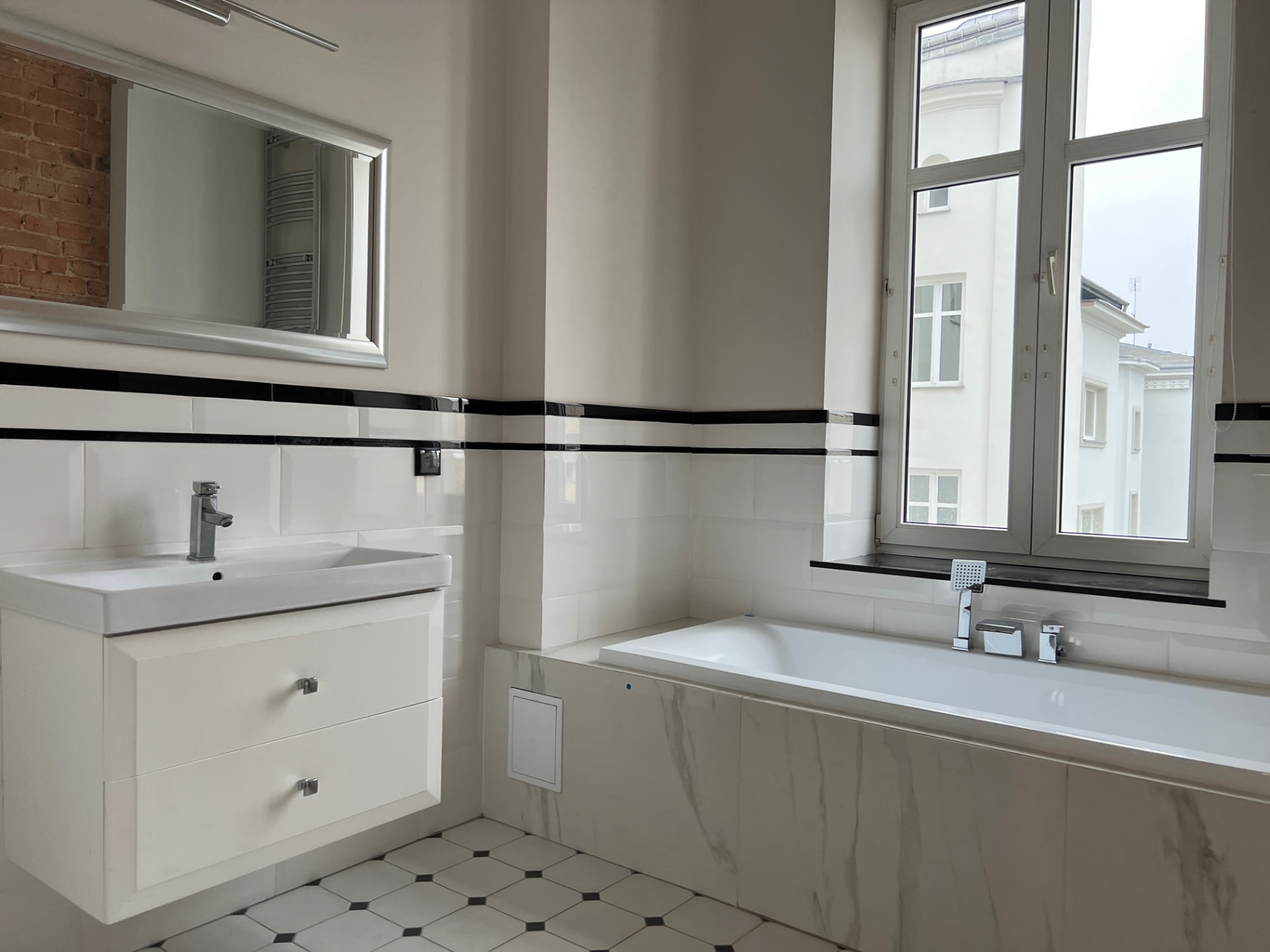Łazienka z wanną w marmurowej zabudowie, umywalką i oknem